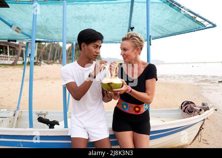 Coppia multiculturale bere un cocco naturale in una spiaggia Foto Stock