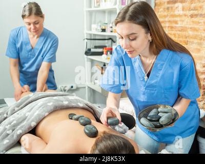 Due massaggiatori che fanno il massaggio completo della pietra del corpo alla giovane donna Foto Stock