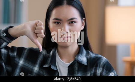 Primo piano asian millennial donna coreana ragazza indossare casual camicia a quadri guardando la macchina fotografica mostrando antipatico pollice giù disaccordo rifiuto rifiuto segno Foto Stock