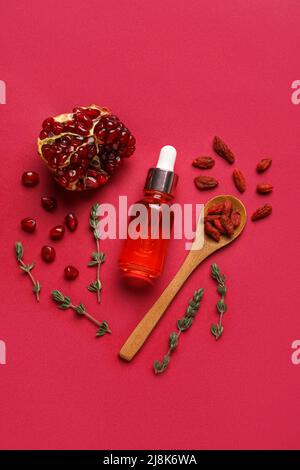 Bottiglia di siero naturale, cucchiaio con bacche di goji, timo e melograno su sfondo rosso Foto Stock