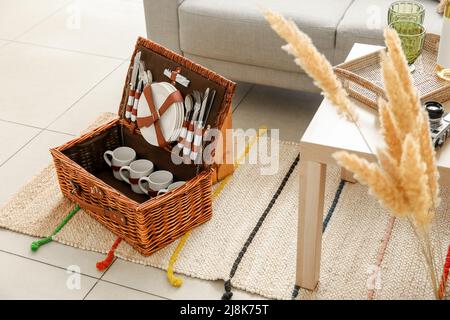 Cestino di vimini con stoviglie per picnic su tappeto in soggiorno Foto Stock