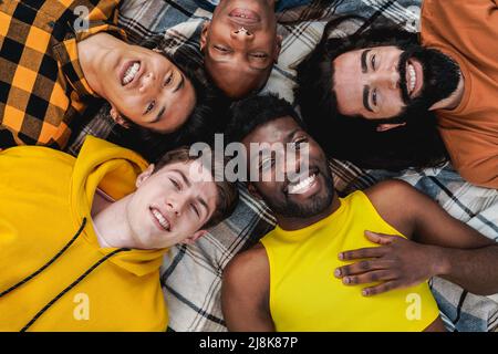 Diversi gruppi di amici alla moda che si divertono insieme all'aperto sdraiati in cerchio - diversità e persone multietniche - Focus on gay man with make up on Foto Stock