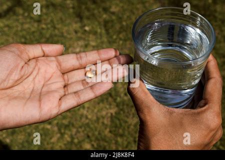 Capsula di vitamina D di colore giallo compresse di gel morbido e sgusciato in mano. Paziente che prende la compressa di integratore vitaminico in mano per mangiare con acqua dolce vetro. Foto Stock