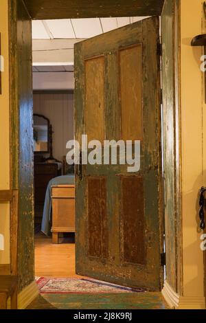 Vecchia camera da letto graffiata e usurata porta in legno all'interno del vecchio regime 1794 francese cottage stile fieldstone casa. Foto Stock