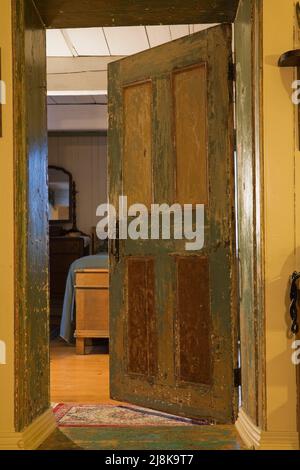 Vecchia camera da letto graffiata e usurata porta in legno all'interno del vecchio regime 1794 francese cottage stile fieldstone casa. Foto Stock