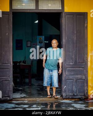 Un proprietario di negozio si trova all'interno della porta del suo negozio aperto, che è buio. Foto Stock