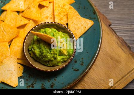 Piatto di nachos chips con salsa guacamole. Utensili fatti a mano. Innaffiatura in bocca. Cibo per feste. Foto Stock