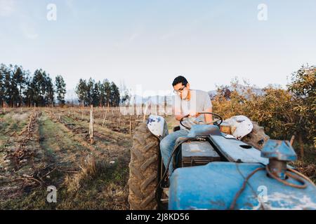 Contadino latino che guida un vecchio trattore, nel mezzo della sua terra. Foto Stock