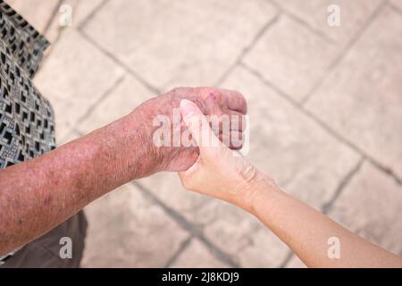 Mano della donna che tiene la mano di un uomo anziano. Concetto di cura per gli anziani. Foto Stock