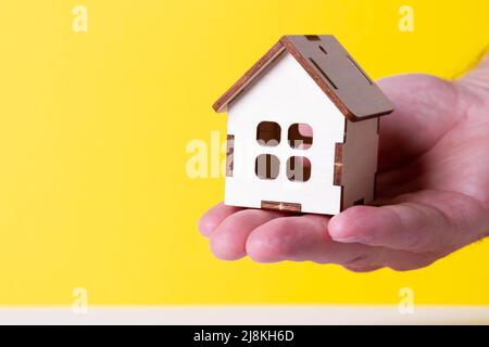 Acquisto di una casa. L'acquirente riceve la chiave per la proprietà. Appartamento ipotecario. Chiavi e una piccola casa in legno in mano. Consegna delle chiavi all'Ora Foto Stock