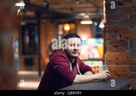 Ritratto di un uomo che beve birra in un bar in stile loft. Vista frontale. Foto Stock