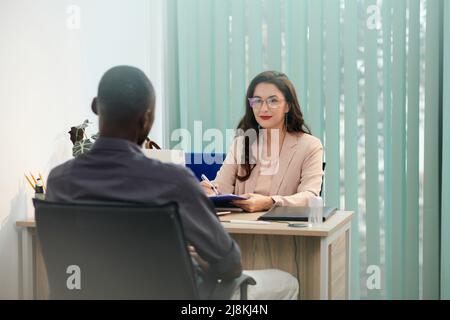 Sorridente responsabile delle risorse umane che parla con il candidato e prende appunti negli appunti Foto Stock