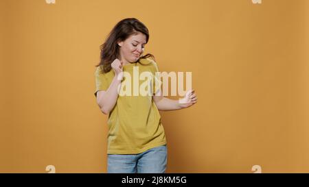 Ritratto di sorridente giovane felice ballare da solo in studio sentendosi fiducioso di muoversi al ritmo della musica. Donna positiva piena di energia che ha partito facendo mosse di danza stravaganti. Foto Stock