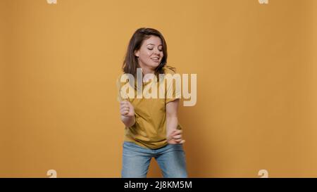 Donna positiva piena di energia ballando da sola in studio sensazione di essere fiducioso nel ritmo della musica su sfondo giallo. Sorridente giovane felice che ha partito facendo le mosse bizzarre di ballo. Foto Stock