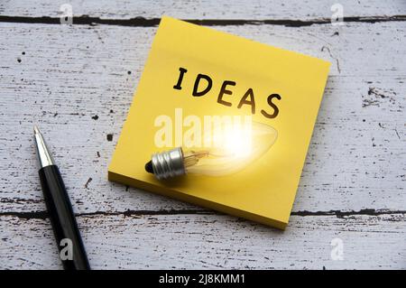 Testo delle idee con lampadina sul blocco note. Scrivania in legno e sfondo penna Foto Stock