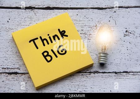 Pensi il testo grande e la lampadina della luce sulla nota della carta. Con scrivania in legno sullo sfondo. Foto Stock