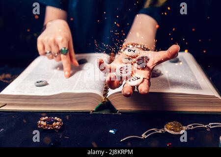 La mano di Fortune Teller tiene le scintillanti pietre zodiacali nel palmo della sua mano sopra il libro aperto. Il concetto di divinazione e magia. Foto Stock