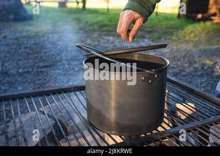 Coperchio di una pentola sul fuoco è sollevato da una mano Foto Stock