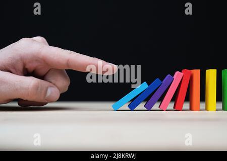 Foto concettuale di una mano che inizia una reazione a catena con dominazioni colorate. Effetto domino con pietre colorate e copyspace. Foto Stock
