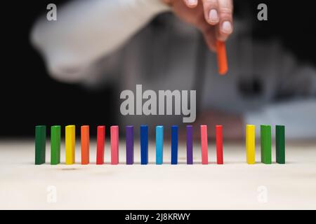 Foto concettuale di una mano che mette una pietra ad una fila di pietre domino. Effetto domino con pietre colorate e copyspace Foto Stock