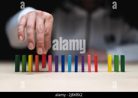 Foto concettuale di una mano che mette una pietra ad una fila di pietre domino. Effetto domino con pietre colorate e copyspace Foto Stock