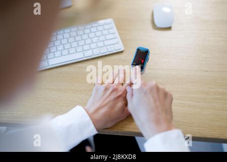 La donna d'affari che lavora in ufficio con un pulsossimetro sul suo dito misura il livello di ossigeno nel sangue Foto Stock