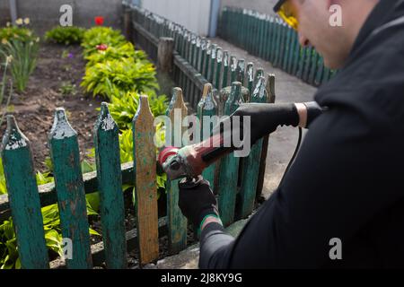 Levigare e preparare una recinzione in legno per la verniciatura. Il padrone sta restaurando vicino alla casa. Foto di alta qualità Foto Stock