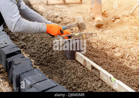 Costruttore che installa blocchi di pavimentazione durante la costruzione di strade e sentieri su calcestruzzo semi-dry mix Foto Stock