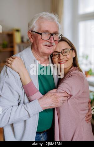 Figlia adulta che abbraccia il padre quando lo visita a casa. Foto Stock