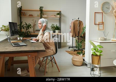 Bella giovane musulmana donna che indossa hijab e cuffie che lavorano da remoto a casa, spazio copia Foto Stock
