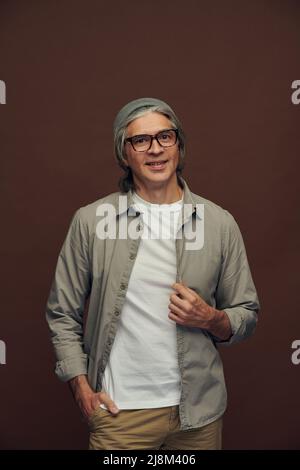 Ritratto di uomo maturo serio e di buona qualità con capelli grigi che indossano cappello da hipter su sfondo marrone Foto Stock
