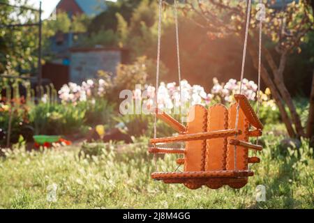 Swing in legno fatto a mano appeso nella scuola materna, sul parco giochi estivo soleggiato. Il concetto della Giornata Internazionale dei Bambini. Foto Stock