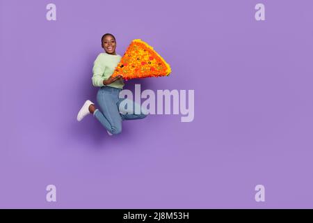 Immagine del corpo pieno della signora ridente overjoyed che mangia la fetta enorme della pizza yummy isolata su sfondo di colore viola Foto Stock