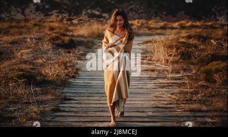 Bella giovane donna che cammina su un sentiero di legno avvolto con un tovagliolo di lana giallo Foto Stock