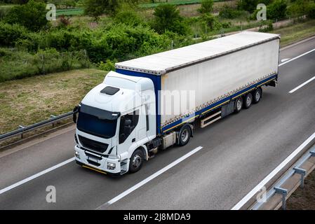 Carro grande potente semi-autocarro industriale bianco professionale per la consegna a lungo raggio carico commerciale che va con semi-rimorchio sulla strada estiva con FORE Foto Stock