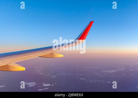 Volo in aereo al tramonto o all'alba. L'ala e la terra dell'aeromobile sono visibili attraverso l'illuminatore. Vista dalla finestra del piano. Aereo, aereo. Traversata Foto Stock