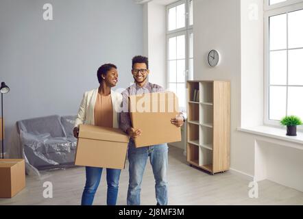 Felice coppia nera che si muove nella loro nuova casa o appartamento e che trasporta le scatole insieme Foto Stock