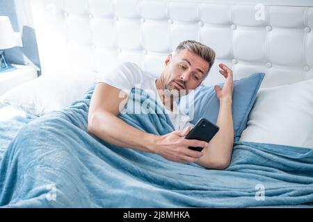 stupito uomo maturo a letto chiacchierando al telefono Foto Stock