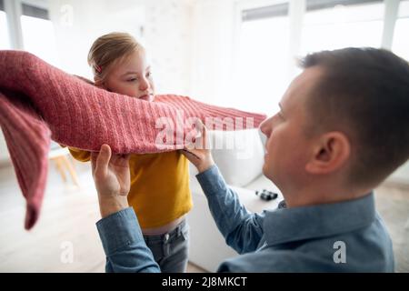 Padre aiutando sua figlia con sindrome Down a indossare il ponticello a casa. Foto Stock