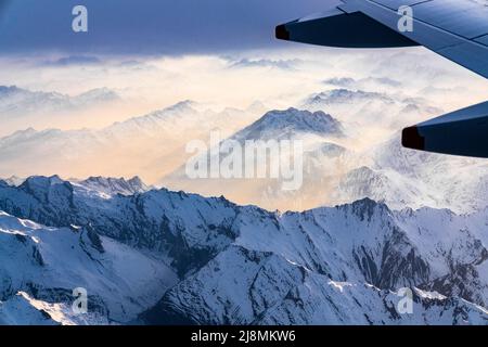 Aereo che vola sulle Alpi Lepontine e Ticino coperto di neve durante un tramonto nebbia, cantone di Graubunden, Svizzera Foto Stock