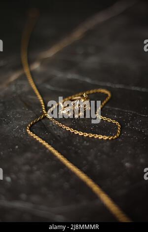 Anello d'oro a forma di coccodrillo con catena d'oro su sfondo di marmo scuro Foto Stock