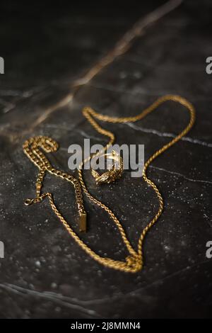 Anello d'oro a forma di coccodrillo con catena d'oro su sfondo di marmo scuro Foto Stock