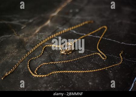 Anello d'oro a forma di coccodrillo con catena d'oro su sfondo di marmo scuro Foto Stock