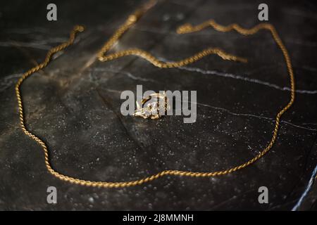 Anello d'oro a forma di coccodrillo con catena d'oro su sfondo di marmo scuro Foto Stock