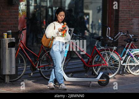 Una donna asiatica che mangia gelato vicino all'entrata del grande magazzino Stockmann. Molti turisti sono venuti a Helsinki nel maggio 2022 a causa del Campionato del mondo di Hockey su ghiaccio. Anche la gente del posto cammina per le strade e goditi il bel tempo. Foto Stock