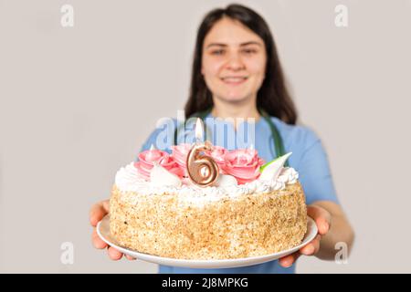 Il medico o l'infermiere tiene una torta di compleanno con il numero sei per l'anniversario dell'apertura della clinica Foto Stock