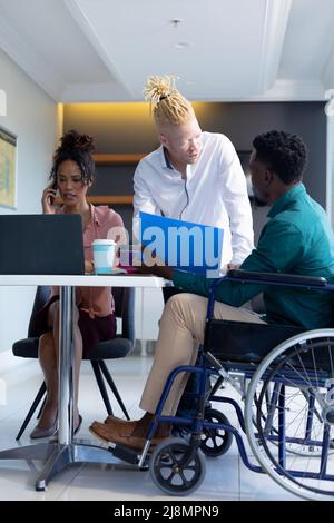 Albino uomo d'affari afroamericano discutere con un collega di sesso maschile seduto su sedia a rotelle in ufficio Foto Stock