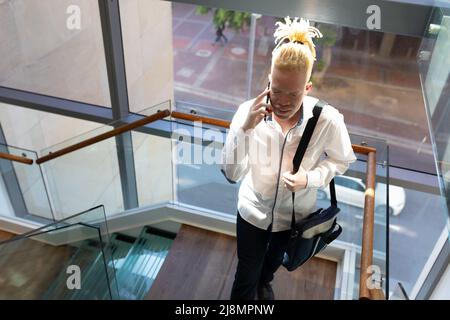 Albino africano americano medio uomo d'affari adulto con borsa che parla al telefono mentre si arrampicano i gradini Foto Stock