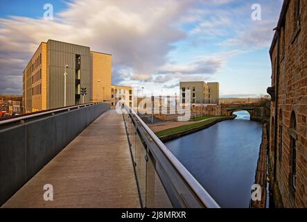 Guardando lungo un ponte pedonale che attraversa il canale di Leeds e Liverpool, verso Sandygate Halls, Burnley College, UCLAN Foto Stock