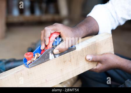 Primo piano mani di Carpenter occupato lavorando utilizzando piano di blocco per la rimozione di superfici ruvide sul legno in negozio - concetto di artigiani, lavoratori autonomi e. Foto Stock